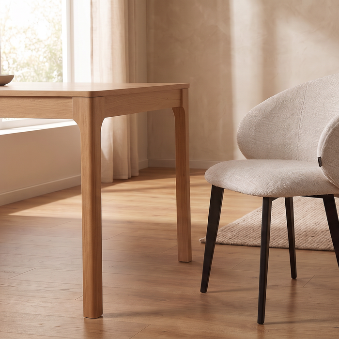 Crèmekleurige LABEL51 Logan eetkamerstoel met zwarte poten naast een houten eettafel in een lichte eetkamer