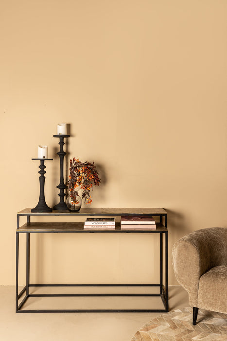 Rechthoekige PTMD bijzettafel Kae met zwart metalen frame en goudkleurig blad van 41x149 cm tegen een beige muur.