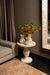 Ronde crèmekleurige Muza bijzettafel van beton met een decoratieve voet, geplaatst in een sfeervol interieur.