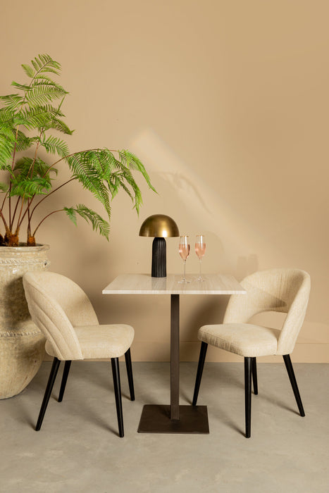 Witte marmeren PTMD eettafel van 70 cm met een slank zwart onderstel, geflankeerd door twee beige gestoffeerde stoelen.