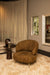 Moderne amberkleurige fauteuil van polyester met een slank metalen onderstel in een sfeervol interieur.