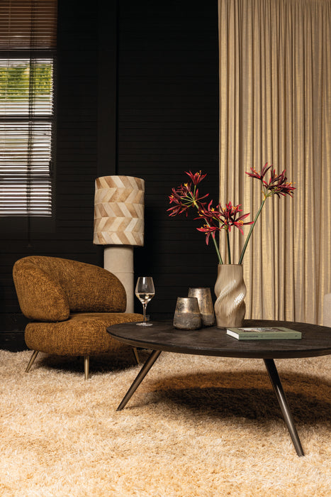 Amberkleurige fauteuil Franklyn van PTMD met polyester bekleding en slank metalen onderstel in een sfeervol interieur.