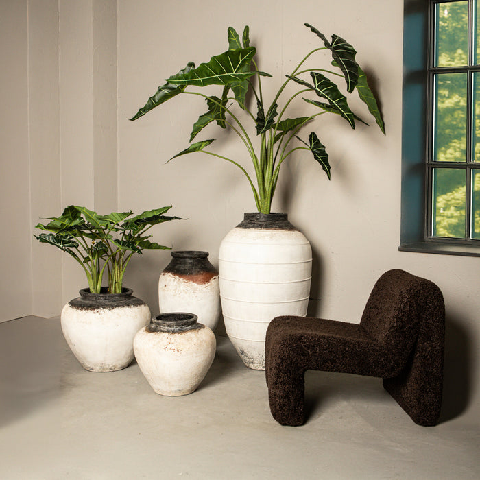 Moderne koffiebruine fauteuil Oslo van PTMD in polyester met een gestructureerde bekleding naast decoratieve vazen.