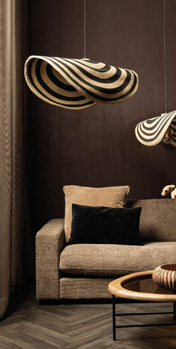 PTMD Loulou hanglamp van rotan met golvend design in naturel en zwart, hangend boven een bank in een sfeervol interieur.