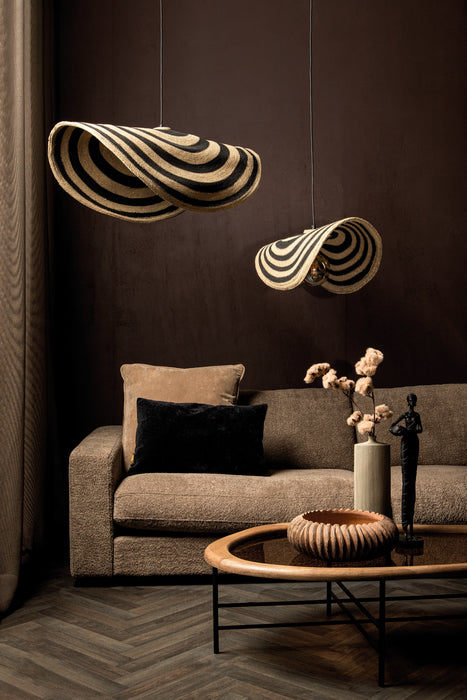 Twee beige en zwarte rotan hanglampen met golvend design boven een bruine bank in een modern interieur.
