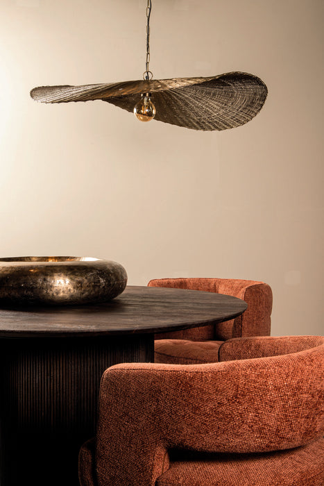 Goudkleurige PTMD Shauney hanglamp van ijzer met golvend design boven een ronde eettafel met oranje stoelen.