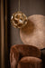 PTMD hanglamp Tijdloze in goudkleurig glas met geometrisch design, 49x49x50 cm, boven een bruine fauteuil.