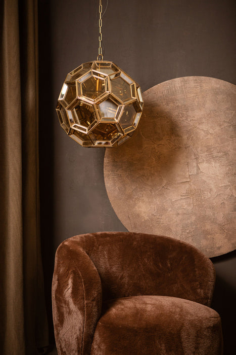 PTMD Tijdloze hanglamp in goudkleurig glas met geometrisch design, 49x49x50 cm, hangend boven een bruine fauteuil.
