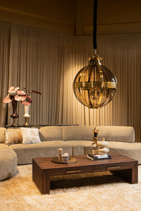 Grote ronde PTMD hanglamp van goudkleurig messing en glas in een sfeervol interieur met bank en salontafel.