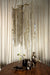 Grote messingkleurige PTMD Wilco hanglamp van 85 cm met decoratieve metalen kettingen boven een houten tafel.