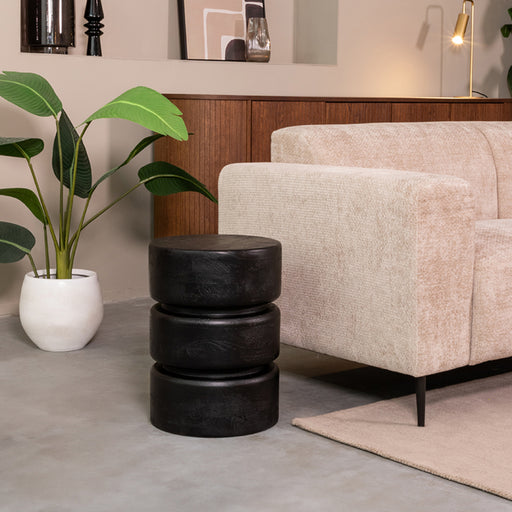 LABEL51 ronde zwarte bijzettafel van mangohout, 35 cm breed, geplaatst in een modern interieur naast een bank.