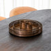 Twee ronde LABEL51 kaarsenhouders van antiek goud metaal met een fijn rasterpatroon op een donkere houten tafel.