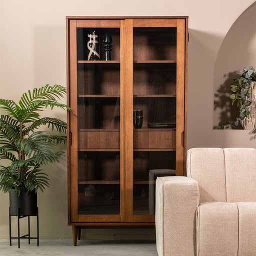 LABEL51 Jule vitrinekast van walnoot eiken met glazen deuren, 100x49x180 cm, in een stijlvol interieur.