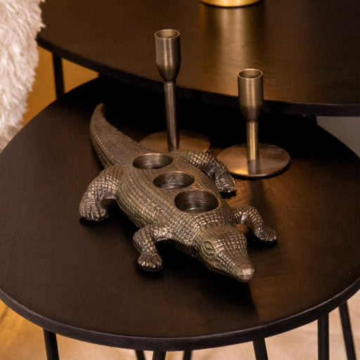 Antiek gouden metalen krokodil waxinelichthouder voor drie kaarsjes, 43 cm lang, op een zwarte tafel.